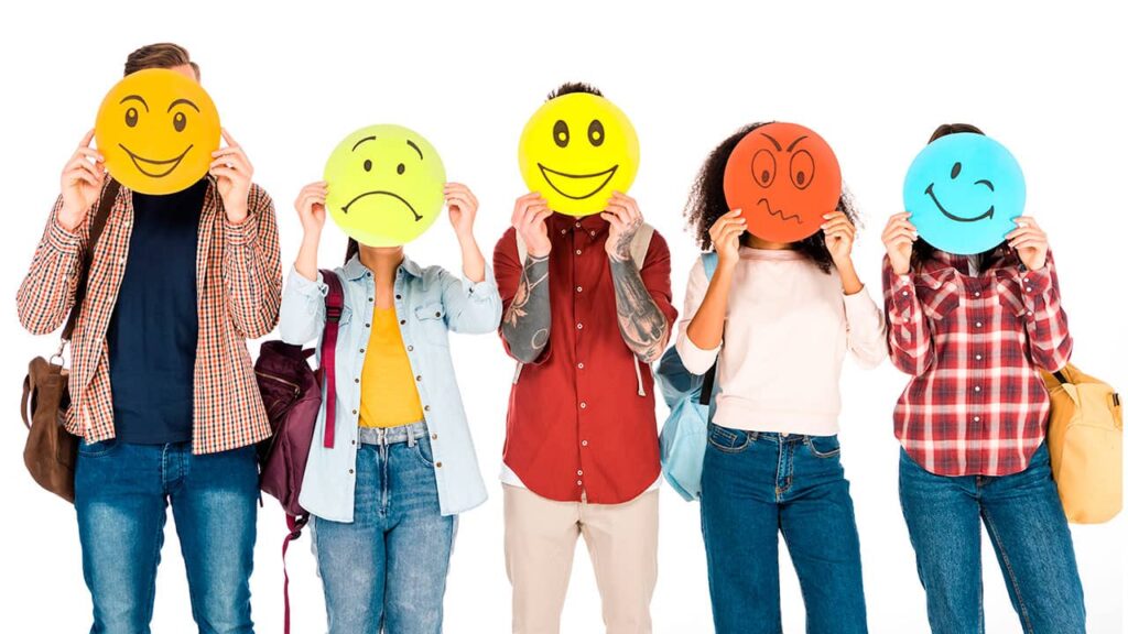 Five individuals standing side by side, each holding up a large circular emoticon face in front of their own, displaying a range of emotions from happy to angry, illustrating the principles of web design psychology.
