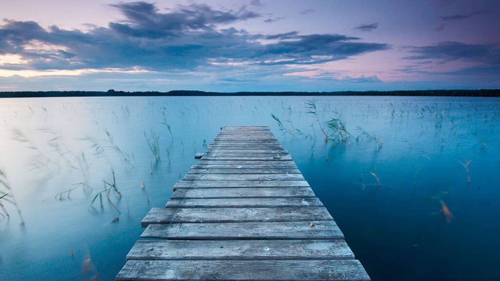 A weathered wooden pier stretches out into tranquil blue waters under a partly cloudy sky at dusk, embodying principles of web design psychology with its calming colors and balanced composition.
