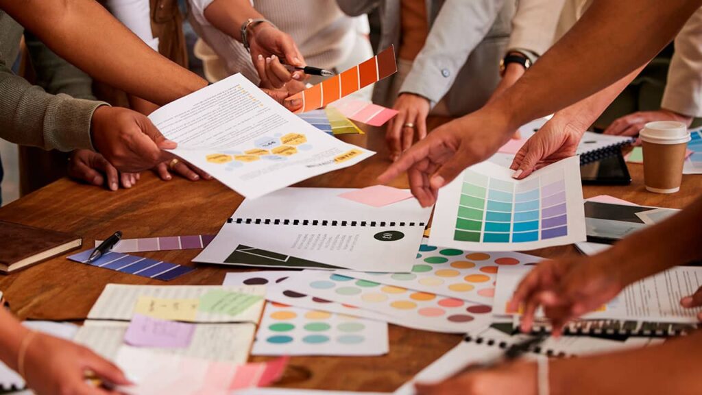 A group of people collaboratively working around a table with color swatches and web design materials.