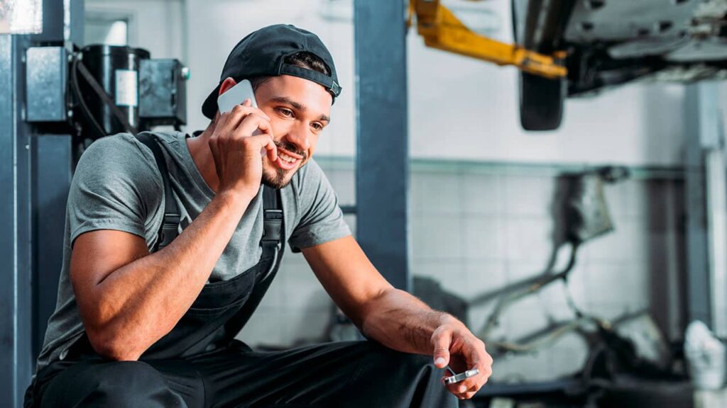 Mechanic having a conversation on a mobile phone about online booking while taking a break in a workshop.